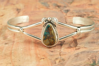 Genuine Royston Turquoise set in Sterling Silver Bracelet. The Royston Turquoise Mine was originally known as the Royal Blue Mine. It produces Turquoise that has a mixture of blues and greens in the same formation. The Royston Turquoise Mine is located in Nye County, Nevada. Created by Navajo Artist Lucy Valencia. Signed L. J. by the artist.